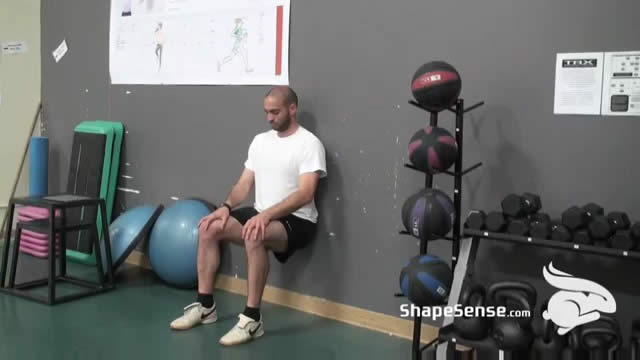 An image of a man performing the wall sit exercise.