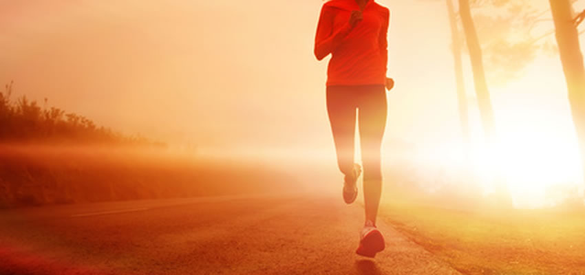 A woman running on a road with the sun behind her.