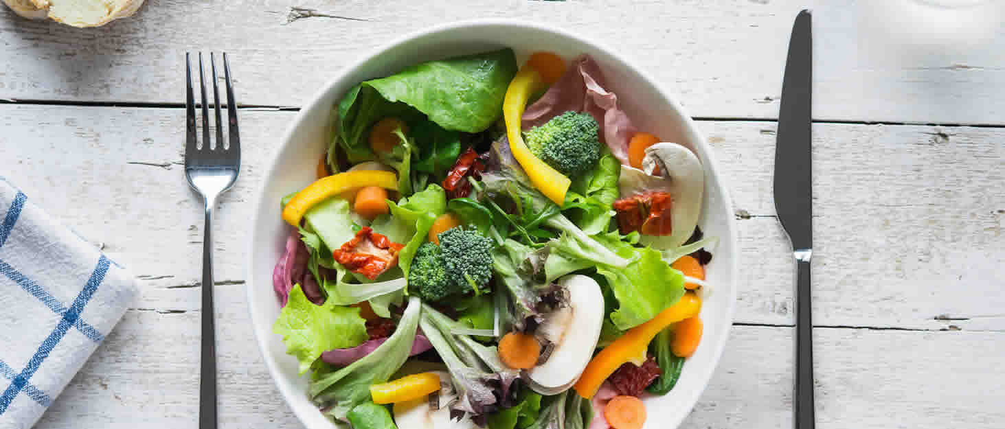 A fresh bowl of salad on a table, ready to eat with knife and fork.